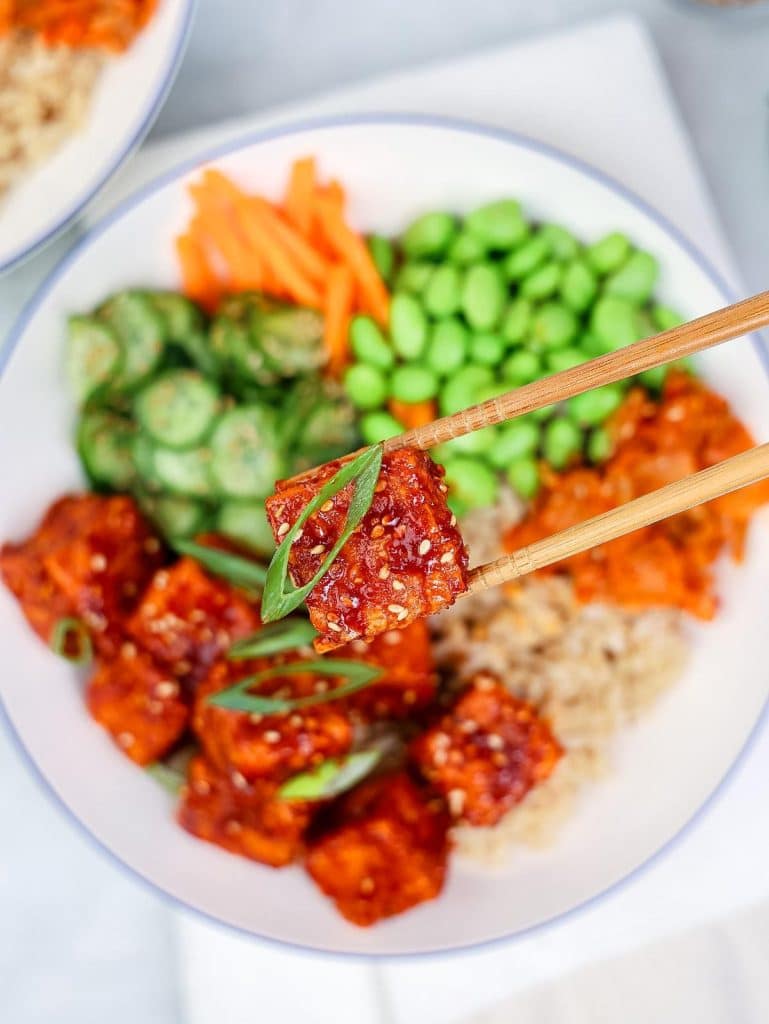Crispy air fryer tofu coated in glossy gochujang sauce held with chopsticks above the bowl