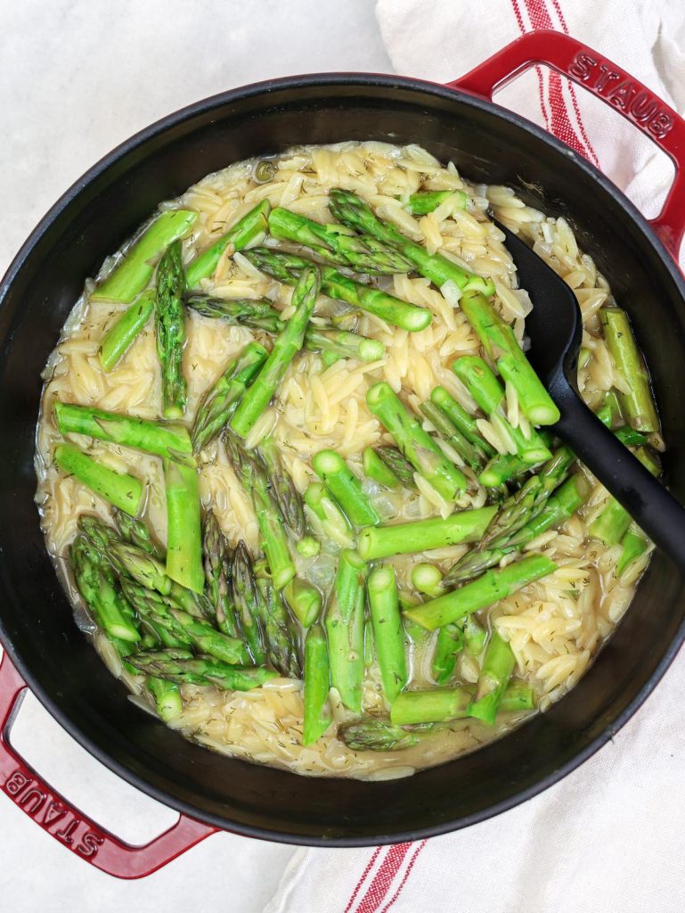 Fresh asparagus scattered over lemon orzo before steaming