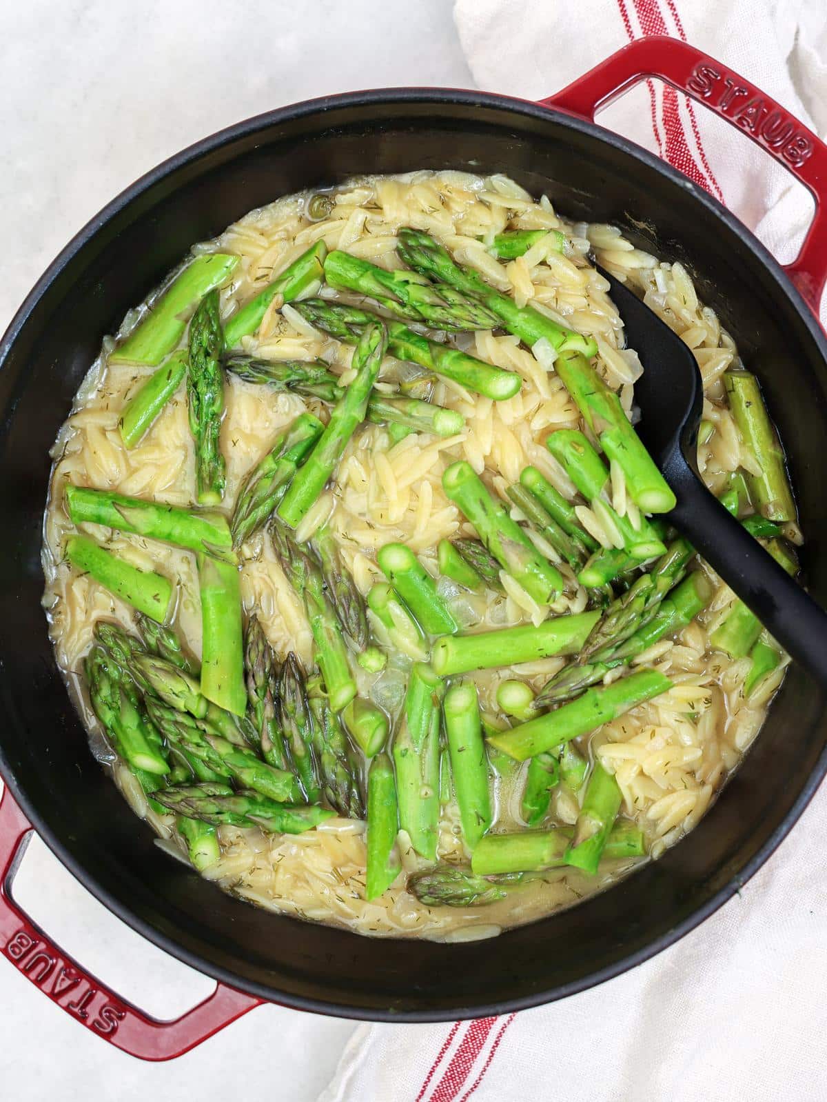 Fresh asparagus scattered over lemon orzo before steaming