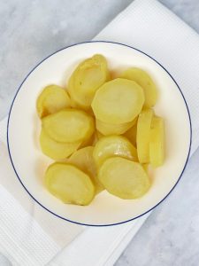Sliced par-cooked potatoes on a white plate for asparagus potato frittata