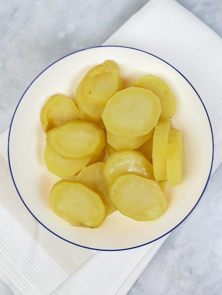 Sliced par-cooked potatoes on a white plate for asparagus potato frittata