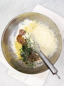 Caesar salad dressing whisked in a metal bowl with tarragon, mustard seeds and lemon zest visible