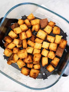 Crispy torn sourdough croutons in an air fryer basket for the caesar salad recipe