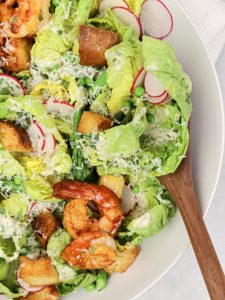 Caesar salad spring version with romaine, peas, asparagus, radishes and parmesan being scooped with a wooden spoon