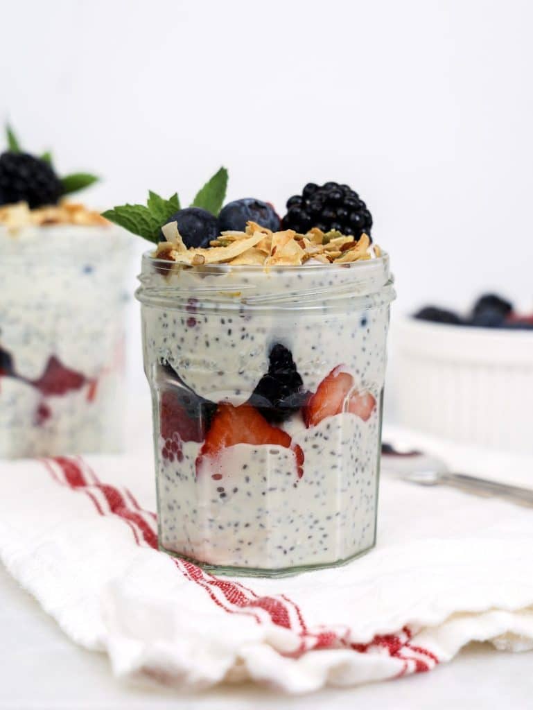 Chia seed yogurt parfait recipe in a glass jar topped with blackberries, blueberries, mint, and toasted coconut
