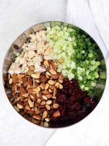 Diced rotisserie chicken, celery, green onions, toasted almonds, and dried cranberries in a stainless bowl