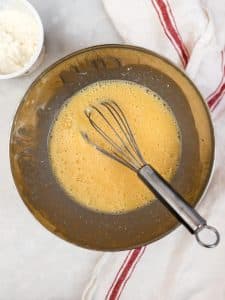 Whisked eggs in a mixing bowl with a tub of cottage cheese, the high-protein base for the scramble