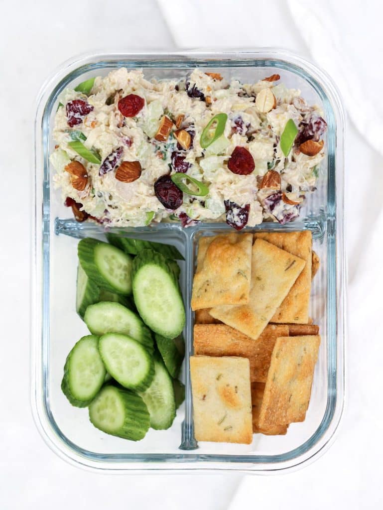 Cranberry almond chicken salad in a meal prep container with sliced cucumber and rosemary crackers