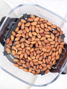 Roasted almonds spread in an air fryer basket, after toasting