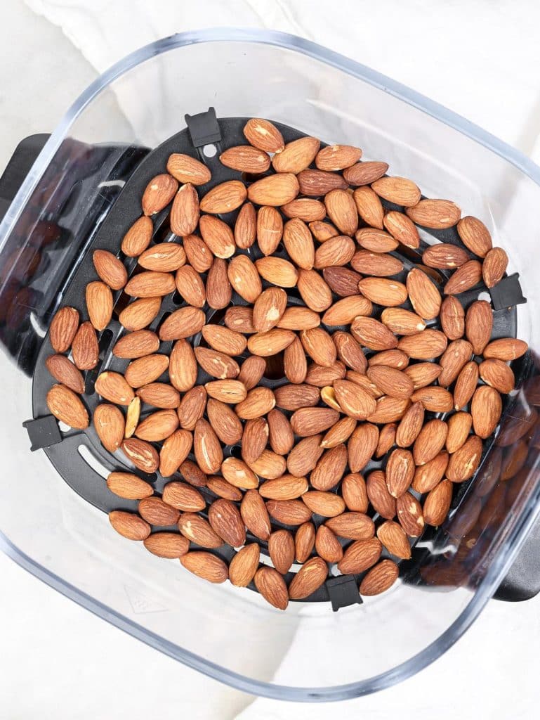 Roasted almonds spread in an air fryer basket, after toasting
