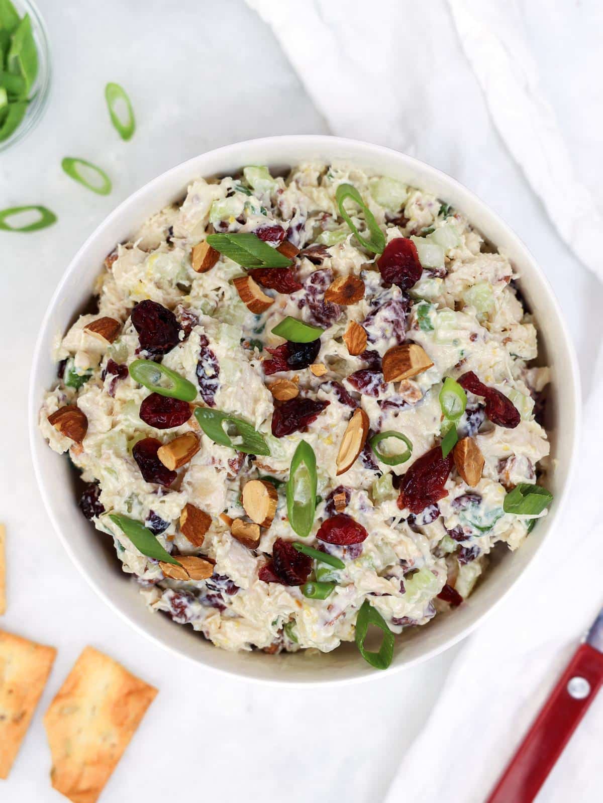 Cranberry almond chicken salad with greek yogurt dressing in a white bowl topped with toasted almonds and dried cranberries
