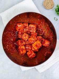 Crispy tofu cubes tossed in glossy red gochujang sauce in a metal bowl