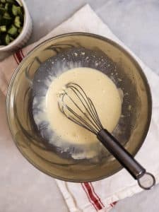 Creamy dill pickle egg salad dressing whisked in a metal bowl with a ramekin of diced spicy pickles