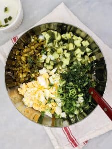 Chopped hard-boiled eggs, diced spicy dill pickles, sliced green onion, and fresh dill in a bowl ready to mix