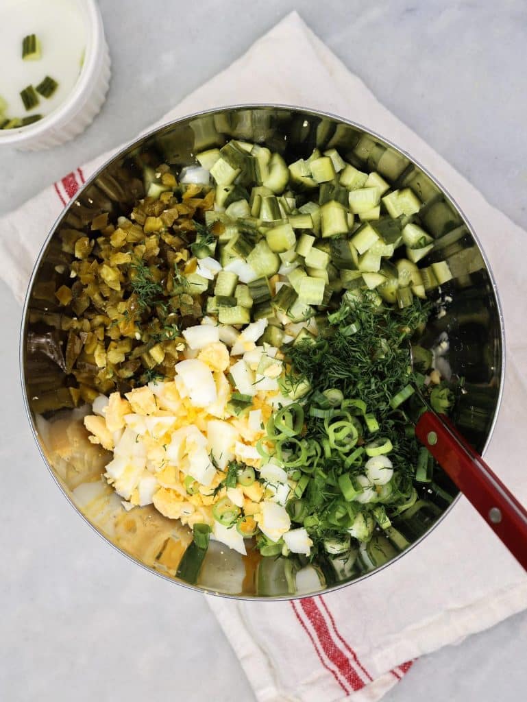 Chopped hard-boiled eggs, diced spicy dill pickles, sliced green onion, and fresh dill in a bowl ready to mix