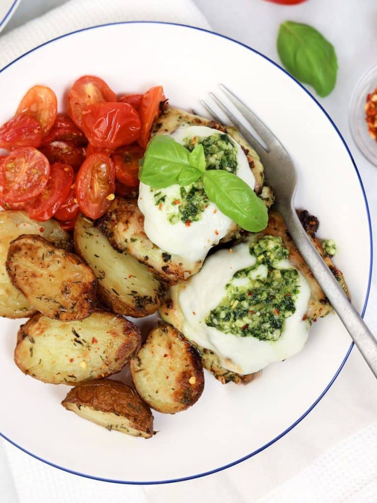 Easy air fryer pesto chicken recipe topped with melted mozzarella, pesto, and fresh basil leaves