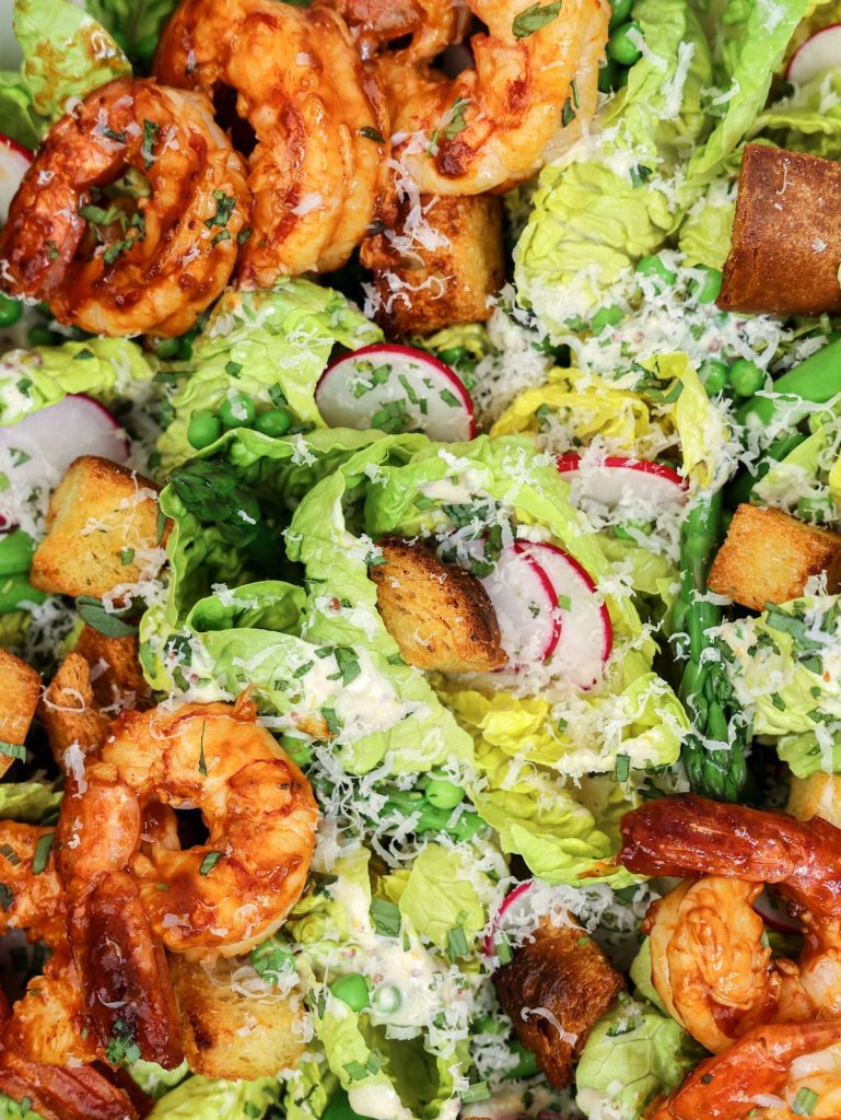 Easy caesar salad spring close-up with grilled shrimp, sourdough croutons, radishes and bright green peas