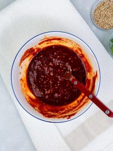 Gochujang sauce mixed in a small white bowl with sesame seeds beside it