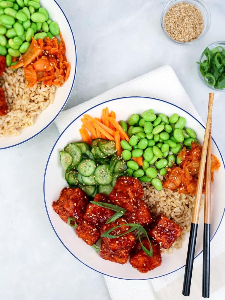Two gochujang tofu bowls with brown rice, edamame, pickled cucumber, shredded carrot, and kimchi