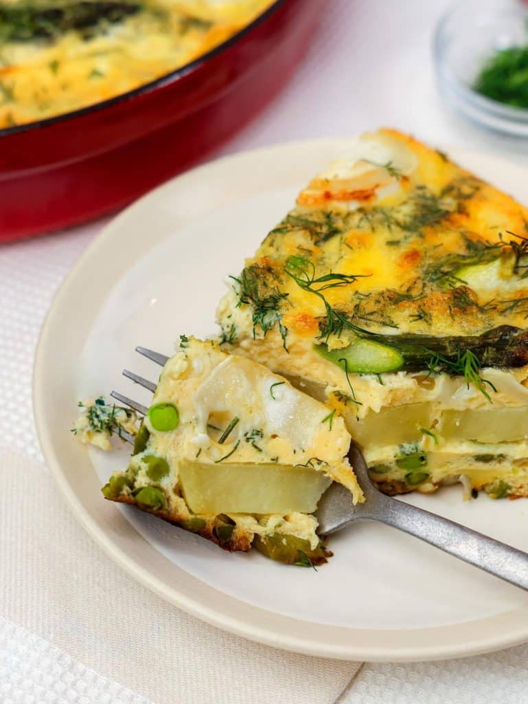 Healthy spring vegetable and goats cheese frittata slice on a plate with fork