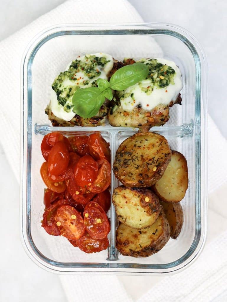 Air fryer pesto chicken meal prep in a glass container with crispy potatoes and cherry tomatoes