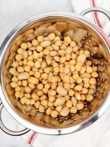 Drained chickpeas and butter beans in a metal colander on a striped tea towel
