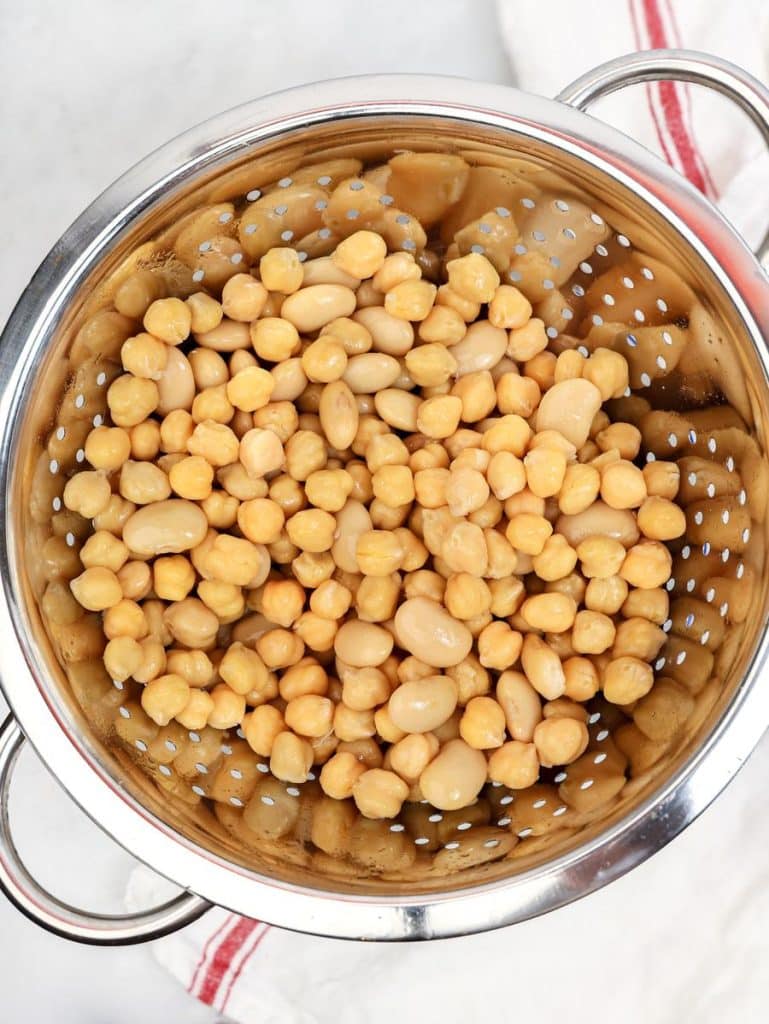 Drained chickpeas and butter beans in a metal colander on a striped tea towel