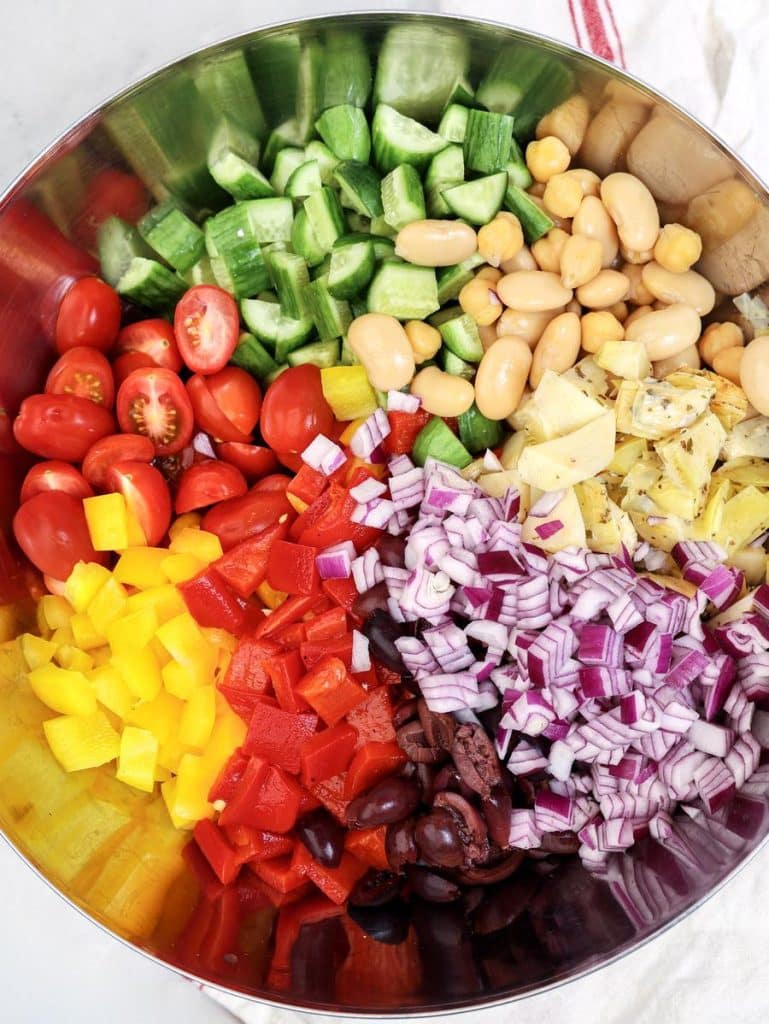 Chopped vegetables and beans arranged in a large metal bowl for Mediterranean dense bean salad