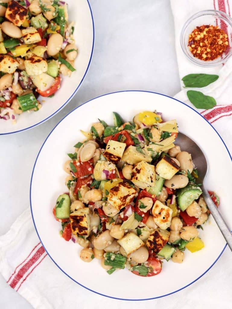 Two plates of Mediterranean dense bean salad topped with fried halloumi cubes