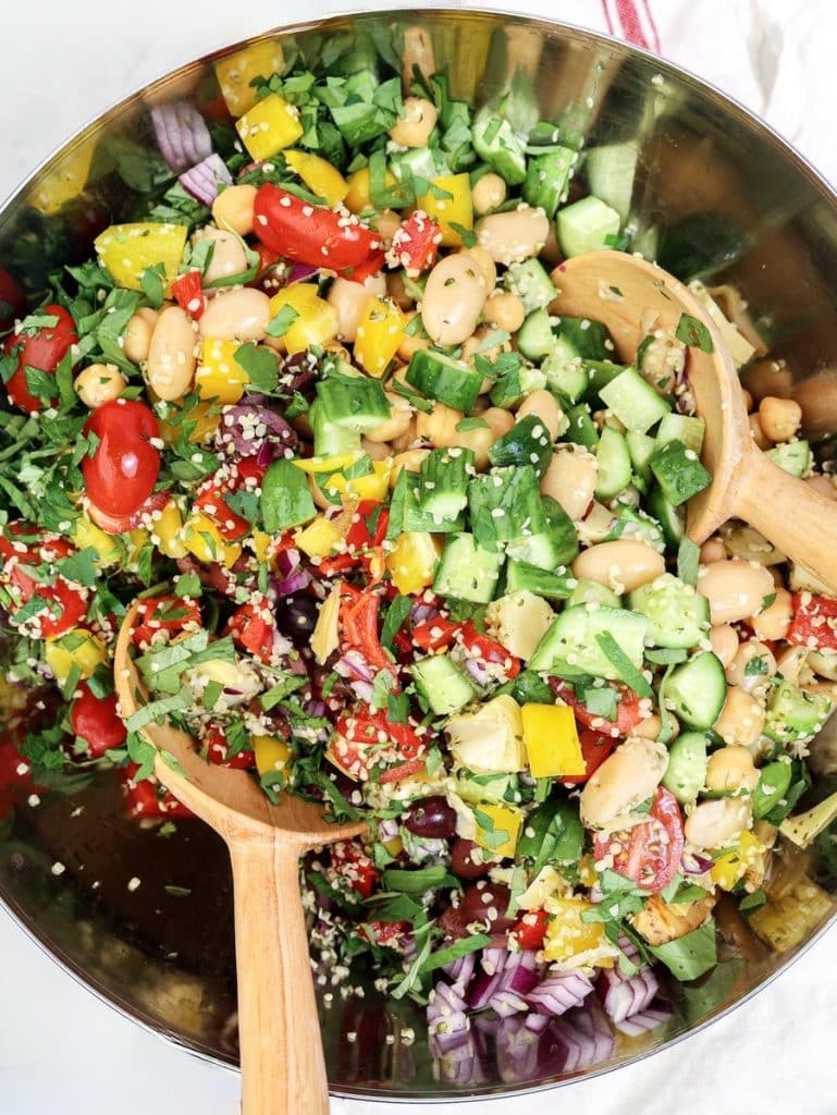 Mediterranean dense bean salad tossed with fresh herbs and hemp hearts in a metal bowl