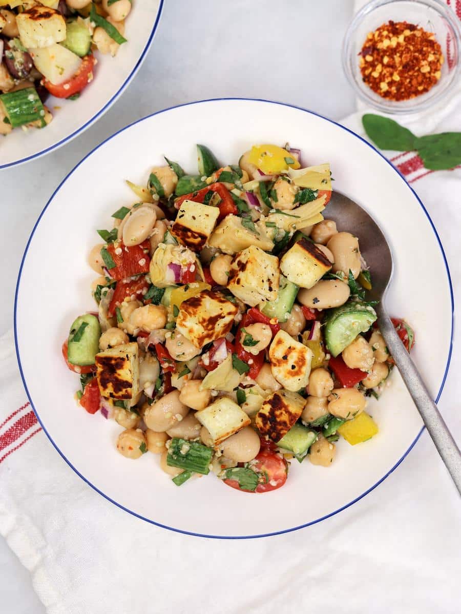 Mediterranean dense bean salad with chickpeas, butter beans, and fried halloumi on a white plate