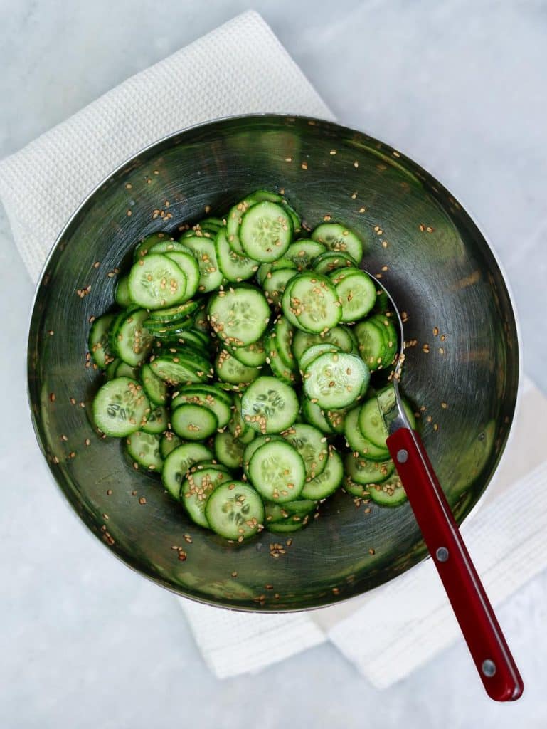 Quick pickled cucumber coins tossed with sesame seeds in a metal bowl