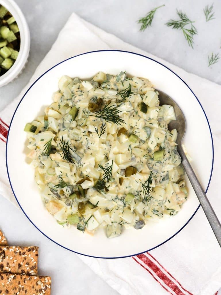 Simple dill pickle egg salad served in a white bowl with seed crackers and fresh dill garnish