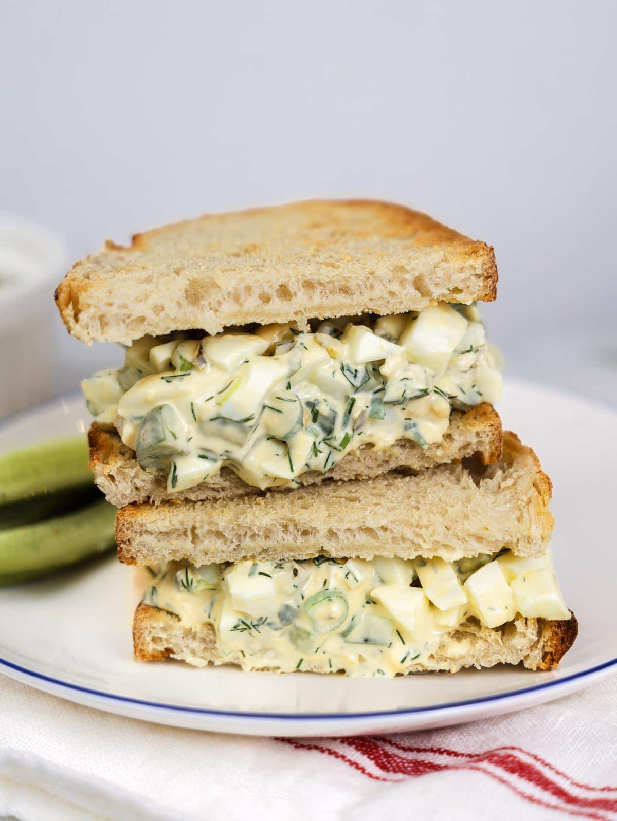 Spicy dill pickle egg salad piled into a toasted sourdough sandwich, stacked and cut in half with pickle spears on the side