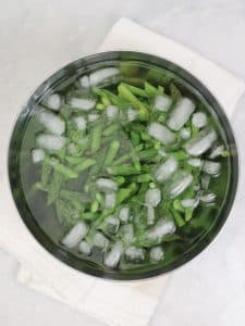 Blanched asparagus pieces shocking in an ice bath for spring caesar salad