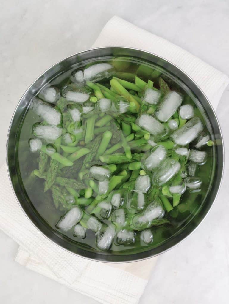 Blanched asparagus pieces shocking in an ice bath for spring caesar salad