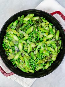Sauteed leeks, asparagus and peas in a red Staub pot for spring green frittata