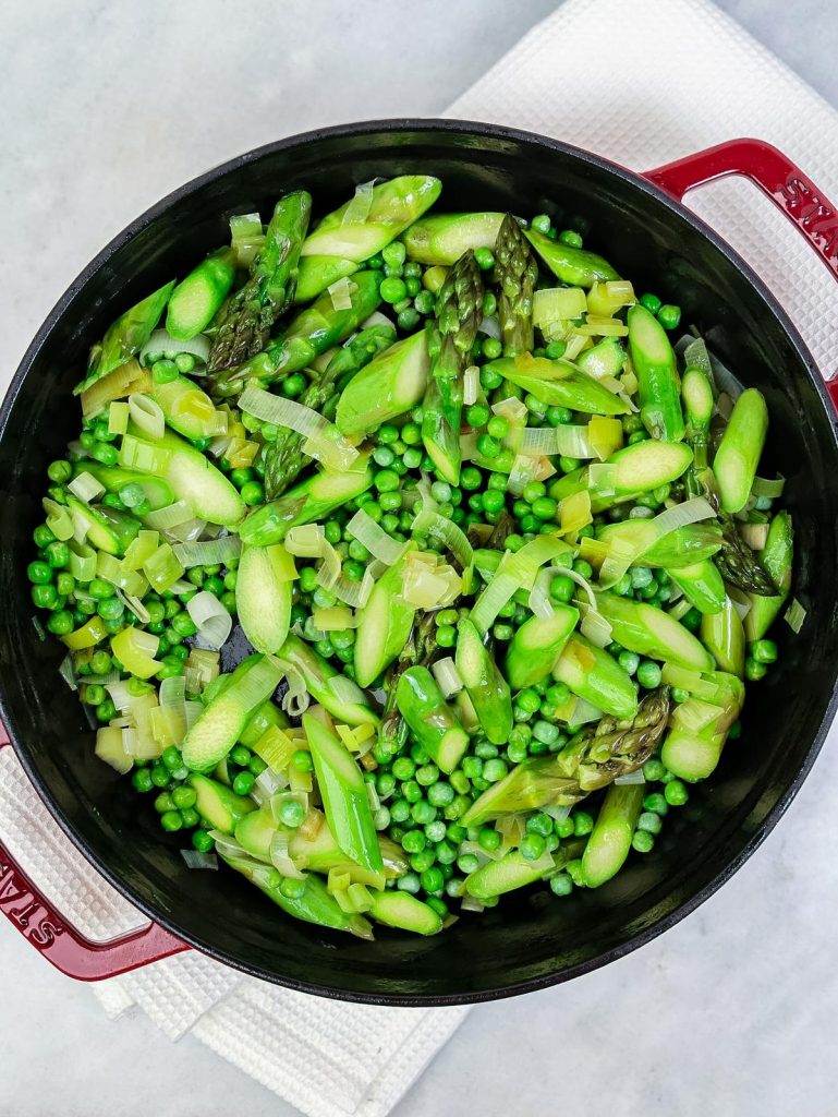 Sauteed leeks, asparagus and peas in a red Staub pot for spring green frittata