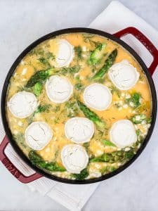 Sliced goats cheese rounds layered over raw eggs and spring vegetables