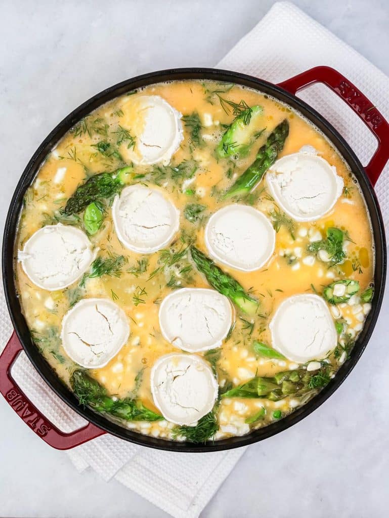 Sliced goats cheese rounds layered over raw eggs and spring vegetables