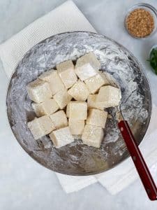 Cubed extra firm tofu tossed in cornstarch dredge in a metal bowl