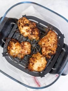 Four marinated lemongrass chicken thighs with charred edges fresh out of the air fryer basket