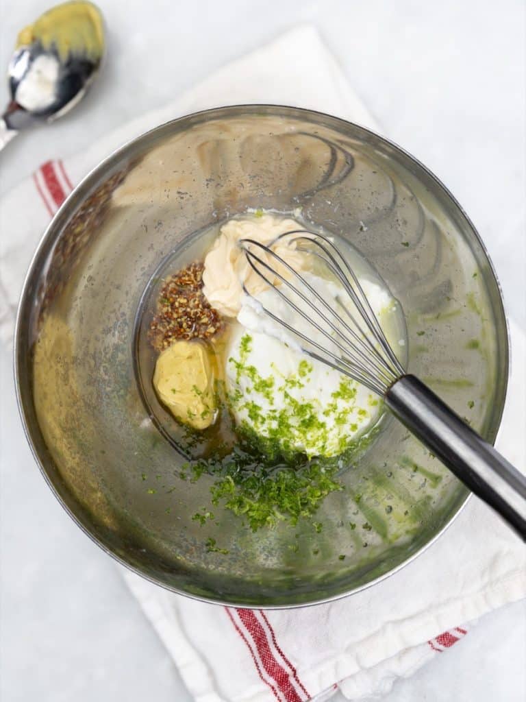 Creamy mustard dressing ingredients in a metal bowl with a whisk