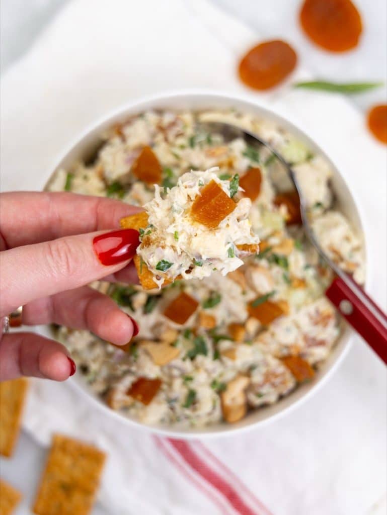 Apricot chicken salad scooped onto a cracker over a white bowl