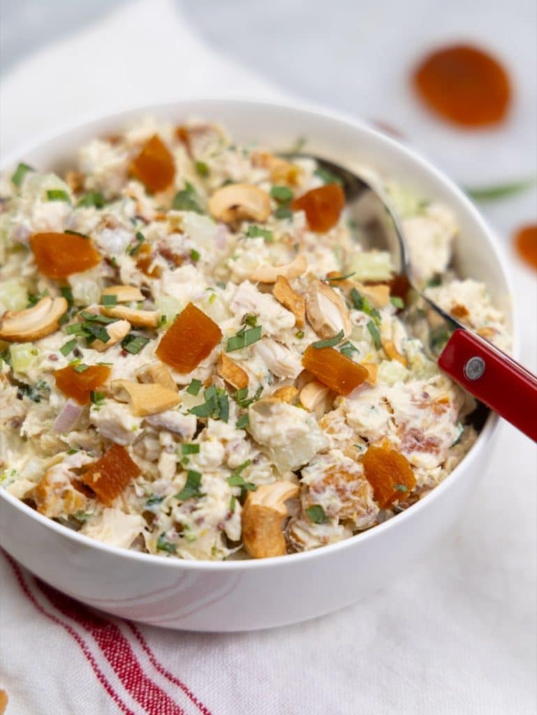 Side view of apricot chicken salad in a white bowl with scattered apricots