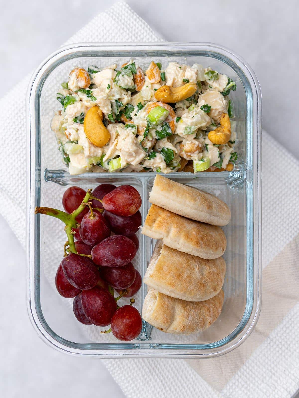 Cashew chicken salad meal prep container with red grapes and rolls