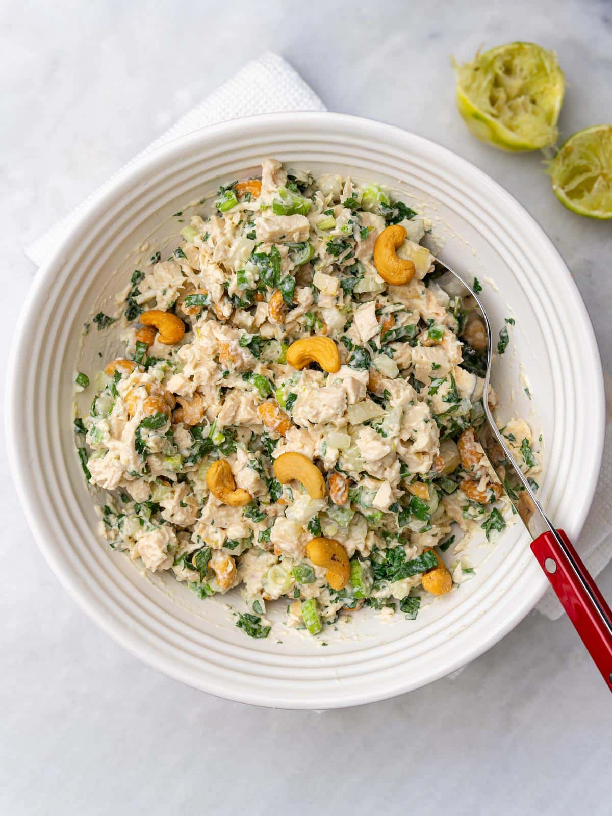 Overhead bowl of cashew chicken salad with toasted cashews and a red spoon