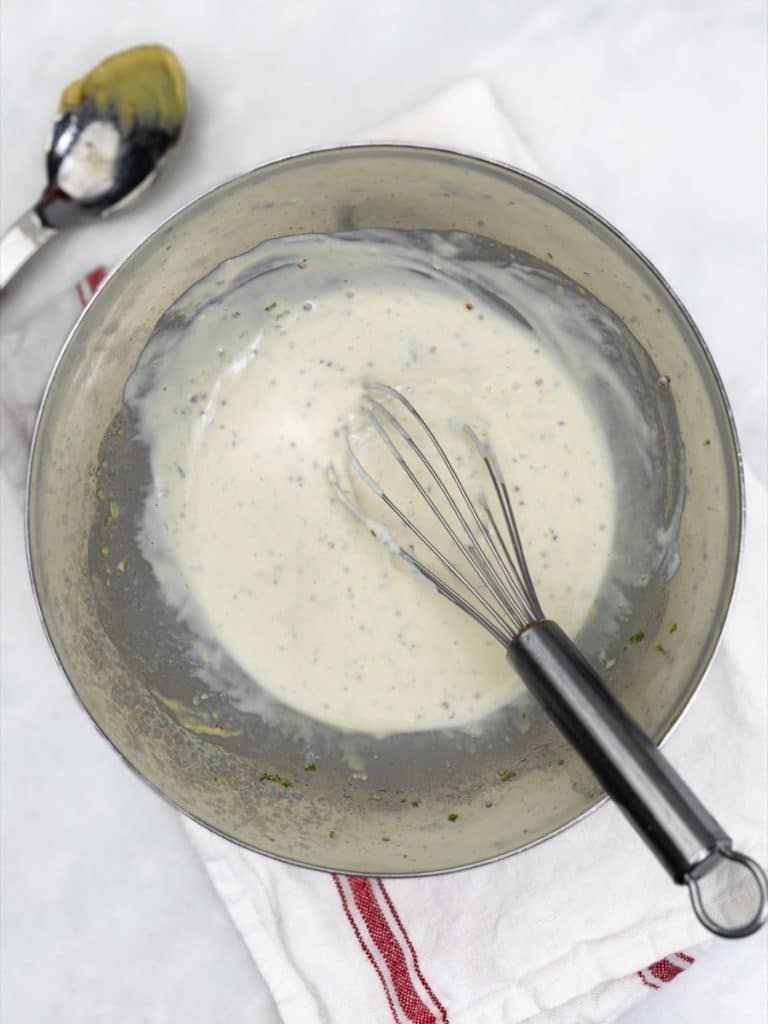 Whisked greek yogurt and mustard dressing in a metal bowl