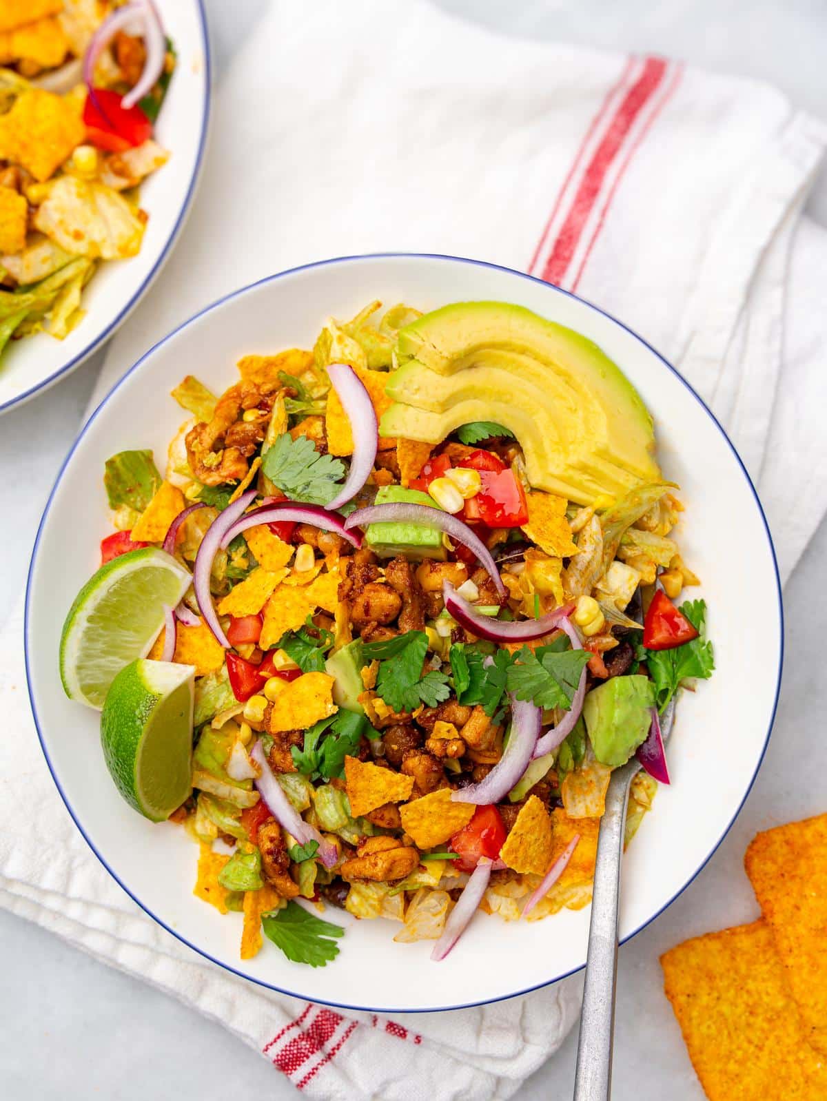 Chicken taco salad bowl with lime wedges, avocado, red onion and tortilla chips