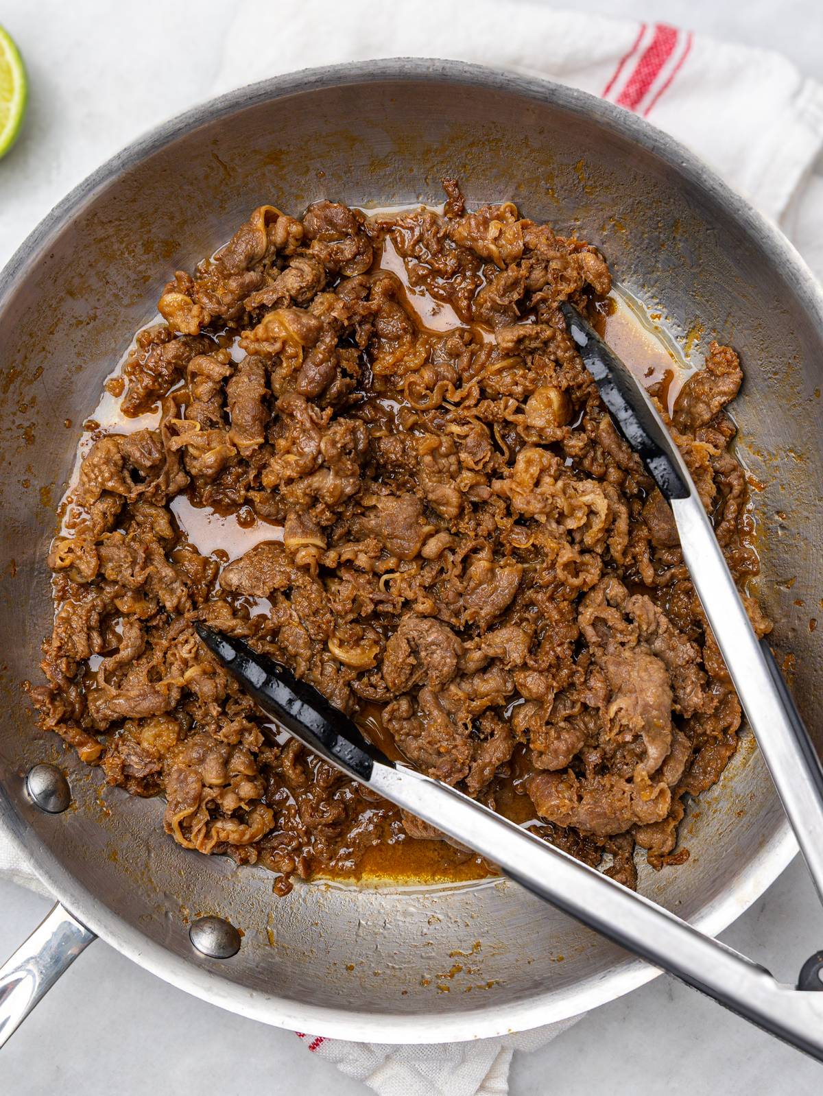 Cooked marinated beef in a skillet with tongs, browned and ready for summer rolls